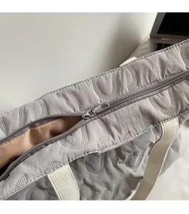 Detail of silver metal zipper and U-shaped quilted texture on light grey tote bag