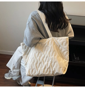 Detailed view of white quilted tote bag featuring elegant S-shaped stitching and side logo