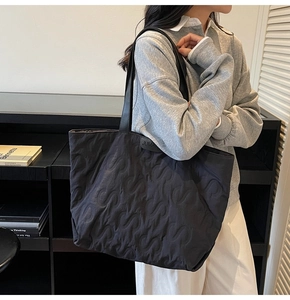 Detail of black quilted tote bag showing S-pattern embroidery and JUMAN leather tag