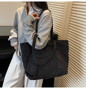 Detail of a black quilted tote bag with Anagram pattern and slender leather straps