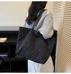 Detail view of the black quilted tote bag featuring an S-shaped embossed pattern and leather tag