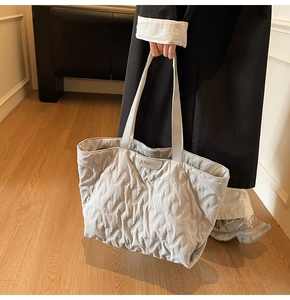 Close-up of light grey quilted tote bag with S-shaped stitching and brand logo tag