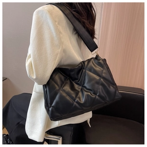 Detail of black quilted shoulder bag with rhombus patterns and wide strap on white blazer