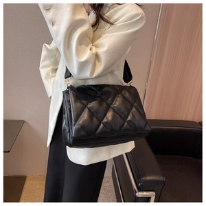 Detail of a black quilted leather shoulder bag with textured finish and wide fabric strap