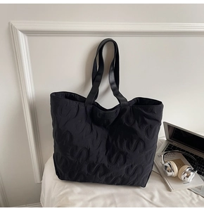 Detail of black tote bag featuring embossed 'S' patterns and leather handles for office