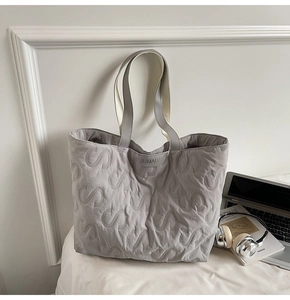 Macro detail of a grey quilted tote bag featuring embossed S-pattern and JUMAITU logo