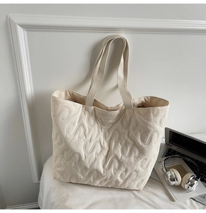 Detail of quilted tote bag with S-pattern texture and brand label near headphones