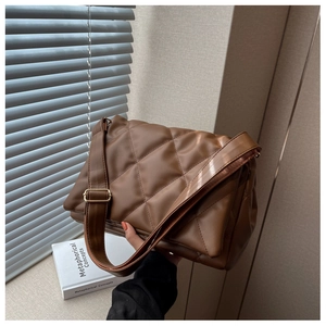 Detail of a brown quilted shoulder bag with large diamond stitching and a wide strap