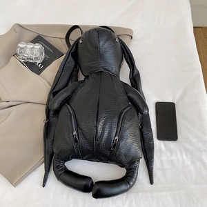 Unique black rabbit shaped backpack in pebbled leather displayed on minimalist bedding