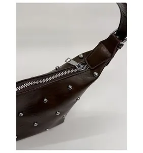 Close-up of smooth silver zipper and metal rivet details on dark brown leather handbag