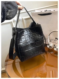 Detail showing high-gloss black crocodile-embossed pattern on a stylish bucket bag