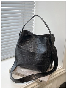 Detail of black crocodile texture bucket bag with wide shoulder strap on a magazine stack