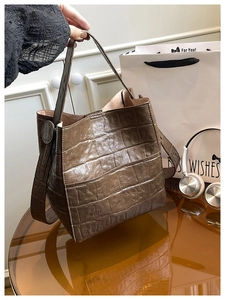 Detail of dark brown faux crocodile bucket bag with glossy texture on a glass table