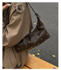 Detail of brown leather underarm bag with silver rivets in an autumn outdoor setting