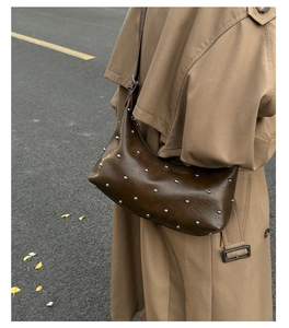 Close-up of vintage brown leather hobo bag with silver studs and ginkgo leaf background