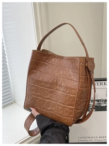 Detail of brown crocodile pattern bucket bag with smooth leather tassels and texture