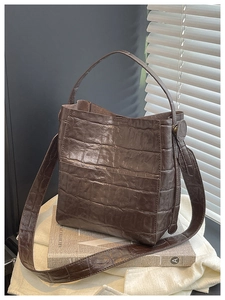 Detailed view of dark brown bucket bag with crocodile texture and shoulder strap