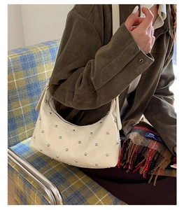 Close-up of beige moon-shaped hobo bag featuring silver rivet studs and zip closure