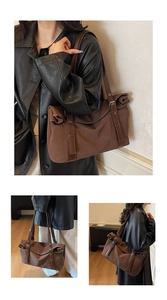 Detail of a large brown tote bag with leather straps and metal buckle on shoulder