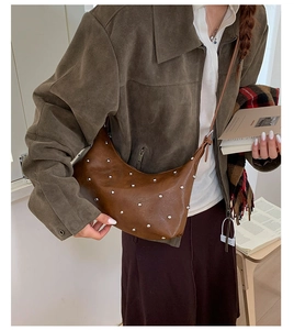 Detail of dark brown crescent bag featuring silver rivets and soft leather texture