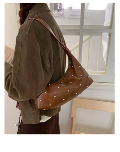 Detail of a brown glossy hobo bag with silver rivets worn over the shoulder