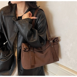 Detail of dark brown tote bag featuring leather straps and decorative buckles on model