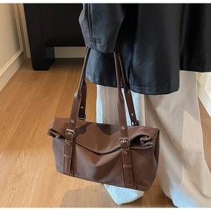 Detail view of large dark brown tote bag with silver buckle worn by model on shoulder