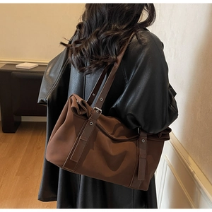 Detail view of brown nylon tote bag with leather straps and silver metal buckles