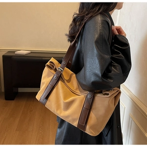 Detail of a large color-block canvas tote bag with brown leather straps and metal buckles