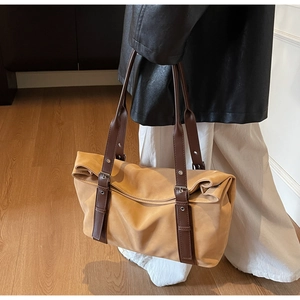 Detail of khaki suede tote bag with brown leather straps on a warm wooden floor