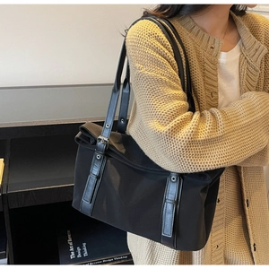 Detail of black nylon tote bag with metal buckle and leather strap on model's shoulder