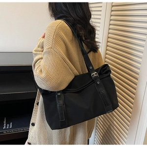 Detail of large black tote bag with nylon texture and leather strap shown on model