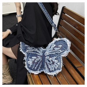 Detail of distressed denim butterfly shoulder bag with raw edges and red stitching