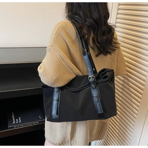 Close-up of a large black canvas tote bag with leather straps on a beige sweater