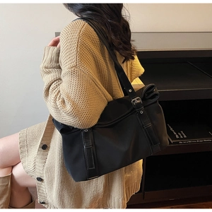 Close-up of black nylon tote bag with metal buckle detail on beige knitted cardigan