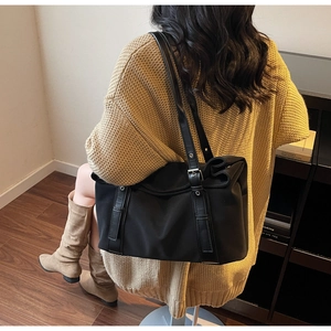 Detail of black large capacity tote bag with leather straps on a yellow sweater