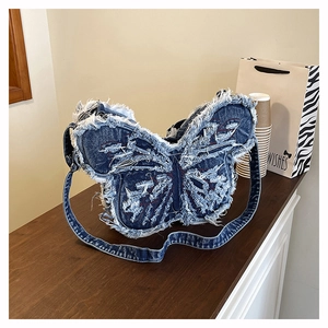 Detail of butterfly-shaped denim crossbody bag with frayed edges and red stitching