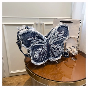 Detailed view of butterfly-shaped denim shoulder bag with fringe and red stitch accents