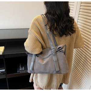 Model wearing a grey suede tote bag with side bow detail and decorative buckle for daily work