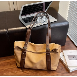Detail of camel tote bag with brown straps and buckle near a laptop in office setting