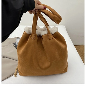 Detail of brown suede bucket bag featuring white faux shearling trim and drawstring handle