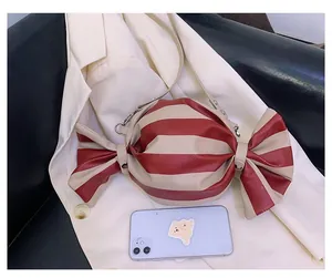 Candy-shaped striped shoulder bag shown next to a smartphone for size comparison