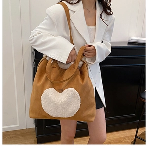 Detail of a large caramel suede tote bag featuring a white plush heart and shoulder straps