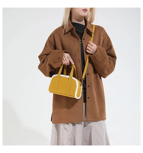 Detail of yellow mini Boston bag with white faux fur trim styled with a brown coat