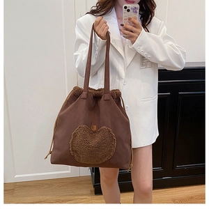 Brown canvas tote bag with plush heart detail shown worn by a model in a white blazer