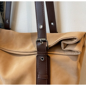 Close-up of camel suede tote bag showing brown leather strap and silver metal eyelet detail
