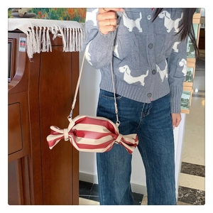 Detail shot of a candy-shaped crossbody bag with red and white stripes on a model