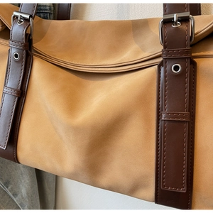 Detail of suede tote bag with brown leather strap, metal buckle and precision stitching