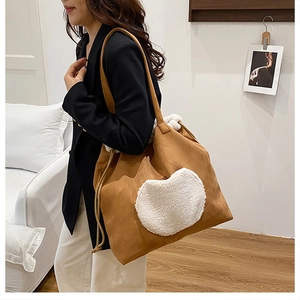 Detail of a brown suede tote bag with a white plush heart and drawstring closure