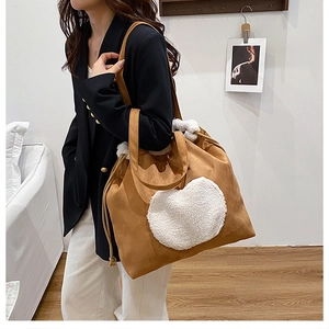 Detail of a brown suede bucket bag with white plush heart applique and drawstring closure